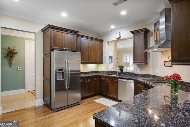 kitchen featuring dark stone countertops, light hardwood / wood-style flooring, decorative columns, appliances with stainless steel finishes, and wall chimney range hood