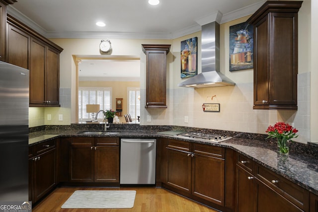 kitchen featuring light wood-type flooring, stainless steel appliances, sink, and wall chimney range hood