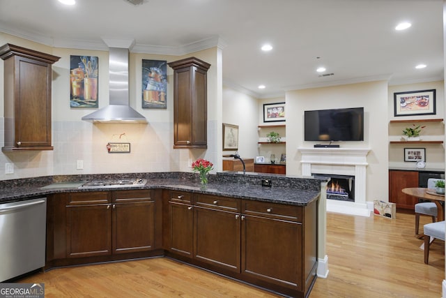 kitchen featuring light hardwood / wood-style flooring, dark stone countertops, wall chimney range hood, and appliances with stainless steel finishes