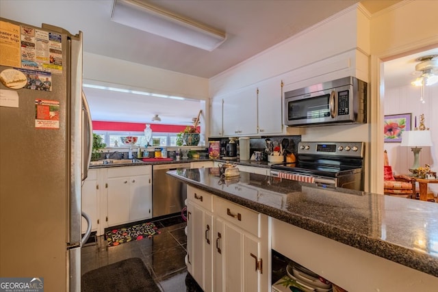 kitchen with appliances with stainless steel finishes, dark tile patterned flooring, white cabinetry, ceiling fan, and dark stone counters