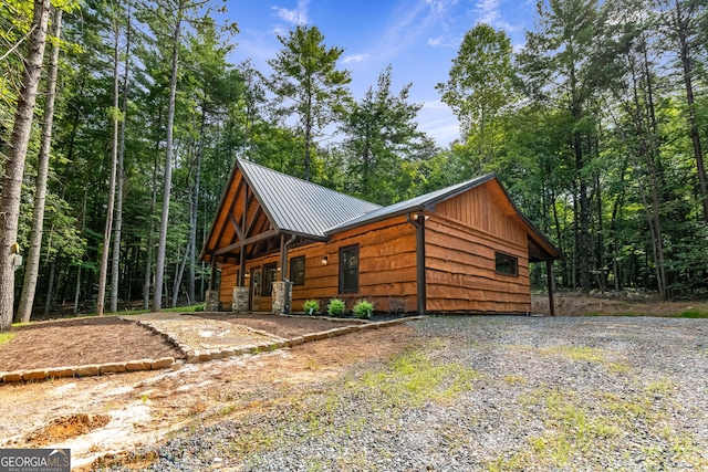 view of side of property featuring metal roof, a standing seam roof, a wooded view, and driveway