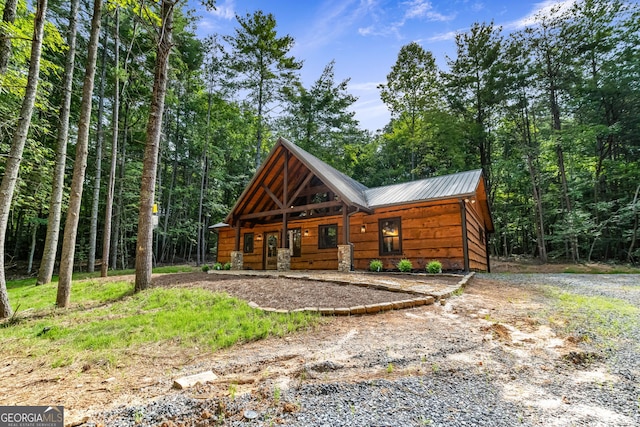 view of front of home featuring driveway, metal roof, and a view of trees