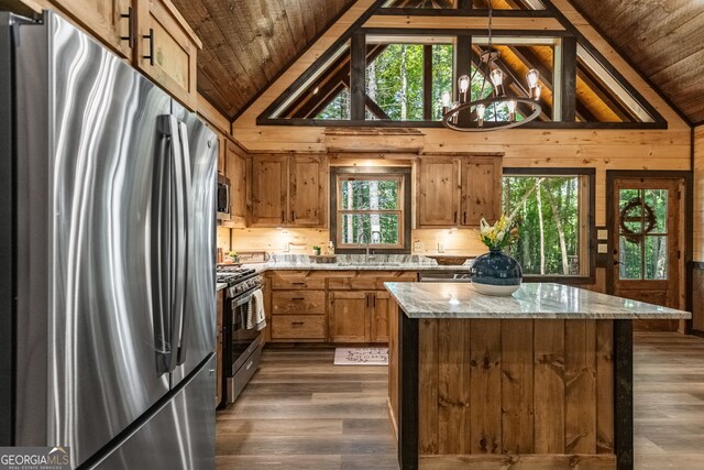 kitchen with light stone countertops, pendant lighting, appliances with stainless steel finishes, a chandelier, and a healthy amount of sunlight