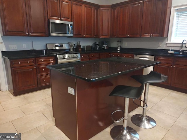 kitchen with light tile patterned flooring, a kitchen breakfast bar, sink, appliances with stainless steel finishes, and a kitchen island