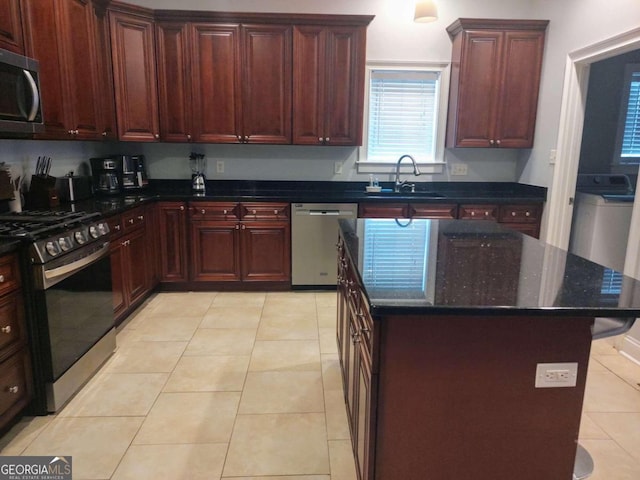 kitchen with light tile patterned flooring, dark stone counters, sink, a kitchen island, and stainless steel appliances