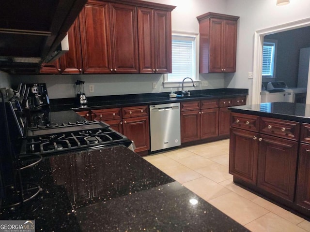 kitchen with sink, stainless steel dishwasher, independent washer and dryer, dark stone counters, and light tile patterned flooring