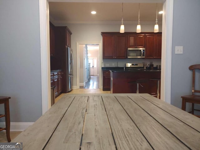 kitchen with appliances with stainless steel finishes, decorative light fixtures, ornamental molding, and light hardwood / wood-style floors