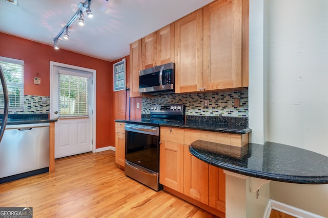 kitchen with light wood-type flooring, stainless steel appliances, decorative backsplash, and a kitchen bar