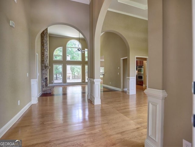 entrance foyer with light wood-type flooring, ceiling fan, a high ceiling, and ornate columns