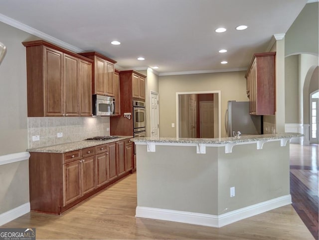 kitchen featuring light stone countertops, light hardwood / wood-style floors, appliances with stainless steel finishes, and a breakfast bar area