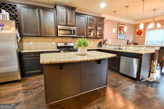 kitchen with dark hardwood / wood-style floors, decorative light fixtures, appliances with stainless steel finishes, a breakfast bar, and kitchen peninsula