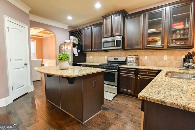 kitchen with dark brown cabinets, crown molding, dark wood-type flooring, stainless steel appliances, and sink