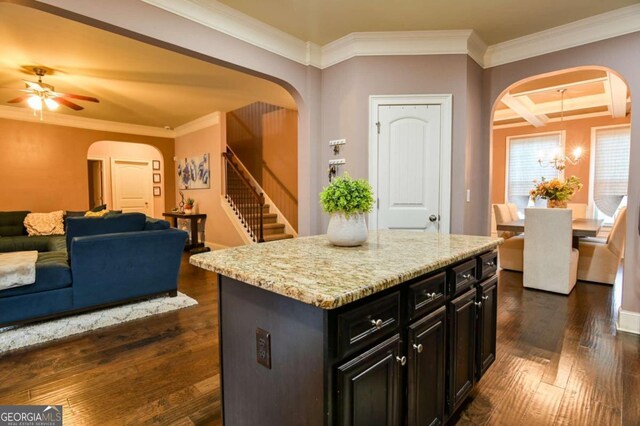 kitchen with ceiling fan with notable chandelier, ornamental molding, a kitchen island, and dark hardwood / wood-style floors