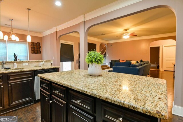 kitchen with ceiling fan with notable chandelier, crown molding, a center island, sink, and dark wood-type flooring