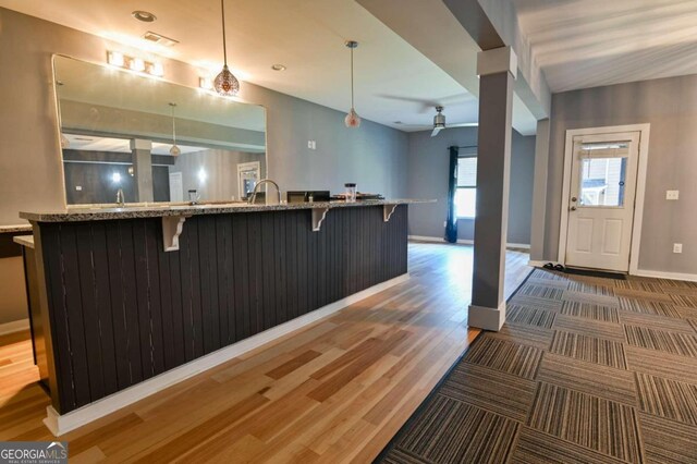 kitchen with hanging light fixtures, light stone counters, wood-type flooring, ceiling fan, and a kitchen bar