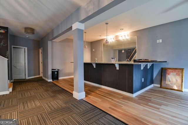 interior space featuring decorative light fixtures, kitchen peninsula, light stone countertops, dark hardwood / wood-style floors, and a breakfast bar area