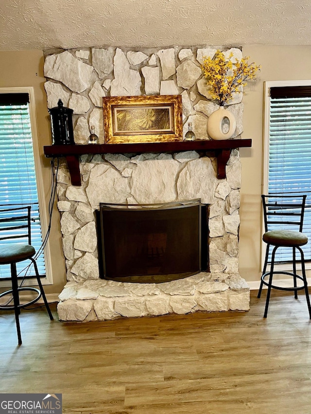 room details with a textured ceiling, hardwood / wood-style flooring, and a stone fireplace