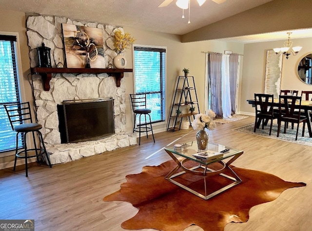 living room with hardwood / wood-style flooring, a textured ceiling, a fireplace, vaulted ceiling, and ceiling fan with notable chandelier