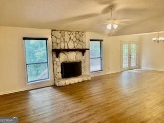 unfurnished living room with ceiling fan with notable chandelier, hardwood / wood-style floors, french doors, a fireplace, and vaulted ceiling