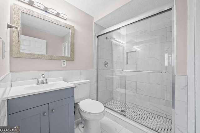 bathroom featuring walk in shower, toilet, tile walls, vanity, and a textured ceiling