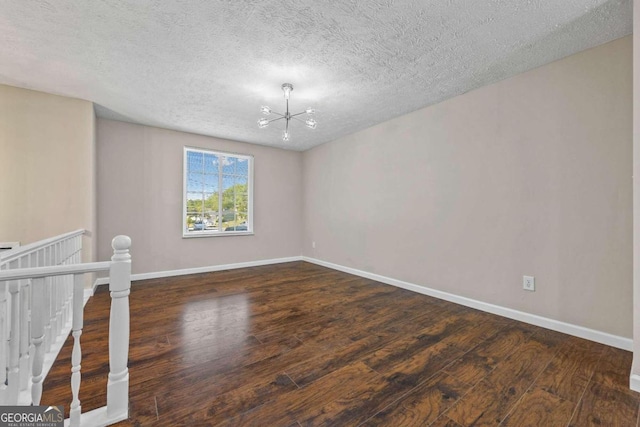 empty room with a textured ceiling, a chandelier, and dark hardwood / wood-style floors