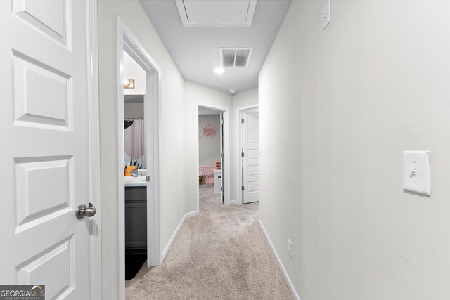 hall with attic access, baseboards, visible vents, and light colored carpet
