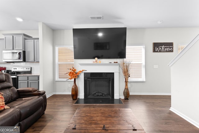 living room featuring a fireplace with flush hearth, baseboards, visible vents, and dark wood-style floors