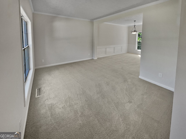 carpeted spare room featuring a textured ceiling, crown molding, and an inviting chandelier