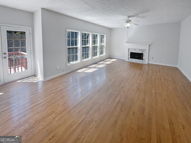 unfurnished living room with plenty of natural light, ceiling fan, light wood-type flooring, and a premium fireplace