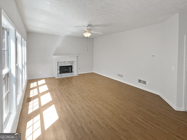 unfurnished living room featuring a high end fireplace, a textured ceiling, hardwood / wood-style floors, and ceiling fan