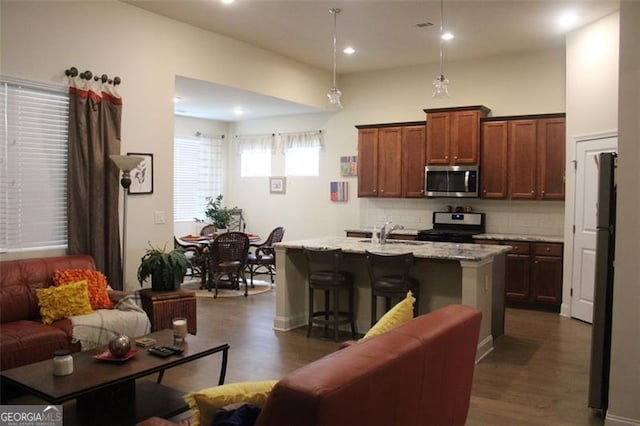 kitchen with appliances with stainless steel finishes, sink, dark wood-type flooring, a breakfast bar area, and a center island with sink