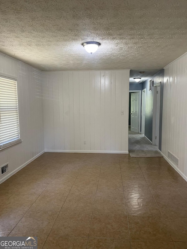 tiled spare room with a textured ceiling and wooden walls