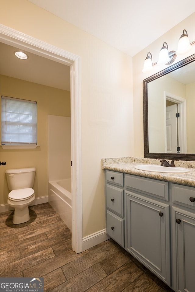 bathroom with wood-type flooring, toilet, a bathtub, and vanity