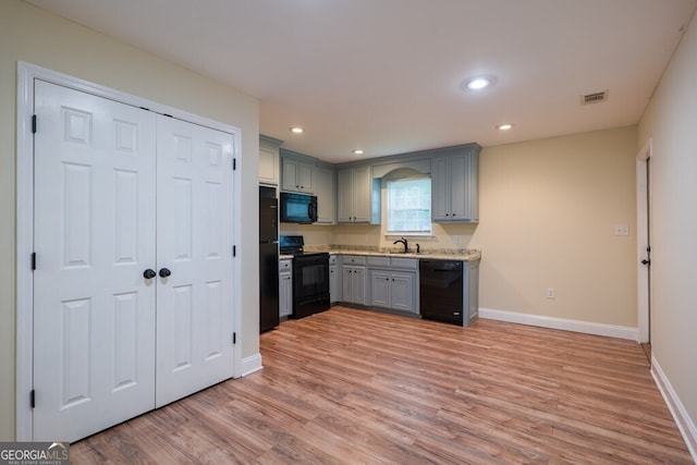 kitchen featuring gray cabinets, light wood-type flooring, black appliances, sink, and light stone countertops