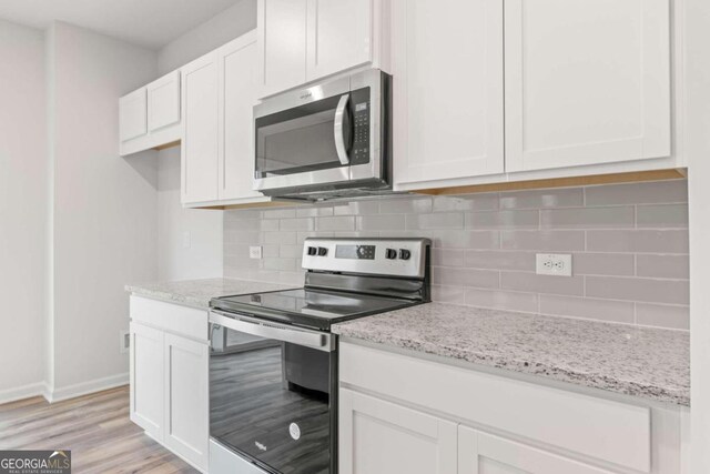 kitchen with light stone countertops, light wood-type flooring, white cabinetry, and appliances with stainless steel finishes