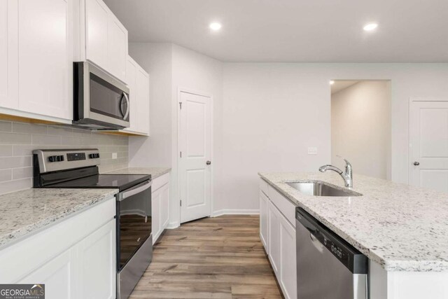 kitchen featuring appliances with stainless steel finishes, light wood-type flooring, light stone counters, sink, and white cabinetry