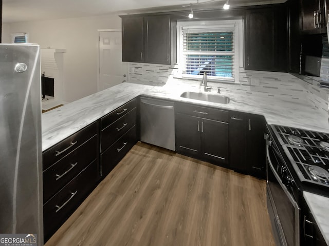 kitchen with stainless steel appliances, wood finished floors, a sink, decorative backsplash, and light stone countertops