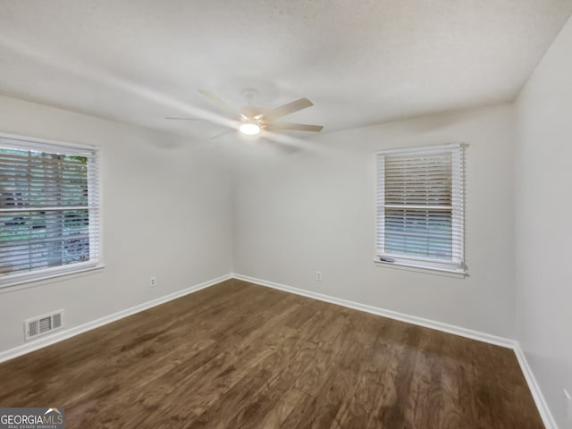 spare room featuring a healthy amount of sunlight, ceiling fan, and dark hardwood / wood-style floors