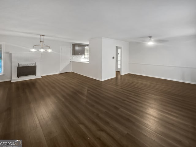 unfurnished living room with dark wood-type flooring, ceiling fan with notable chandelier, and a fireplace