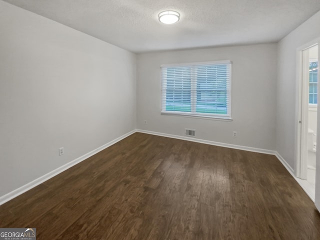 unfurnished room with baseboards, visible vents, dark wood finished floors, and a textured ceiling