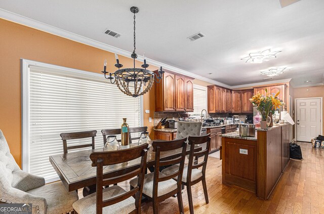 kitchen with backsplash, light stone counters, a chandelier, light hardwood / wood-style floors, and ornamental molding