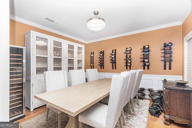 dining area with ornamental molding, beverage cooler, an inviting chandelier, and light hardwood / wood-style floors