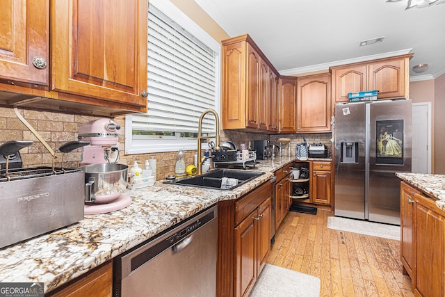 kitchen featuring light wood-type flooring, appliances with stainless steel finishes, sink, tasteful backsplash, and ornamental molding