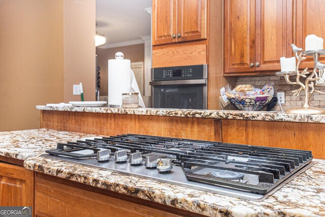 kitchen with crown molding, appliances with stainless steel finishes, tasteful backsplash, and light stone countertops