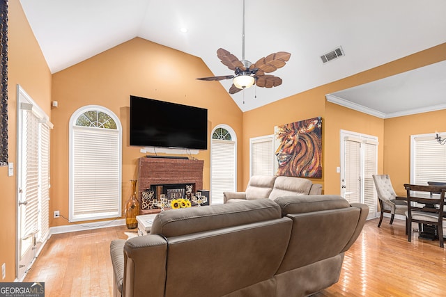 living room with crown molding, high vaulted ceiling, a brick fireplace, ceiling fan, and light wood-type flooring