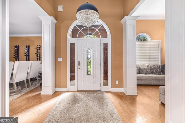 foyer with ornate columns, ornamental molding, a chandelier, and light hardwood / wood-style floors