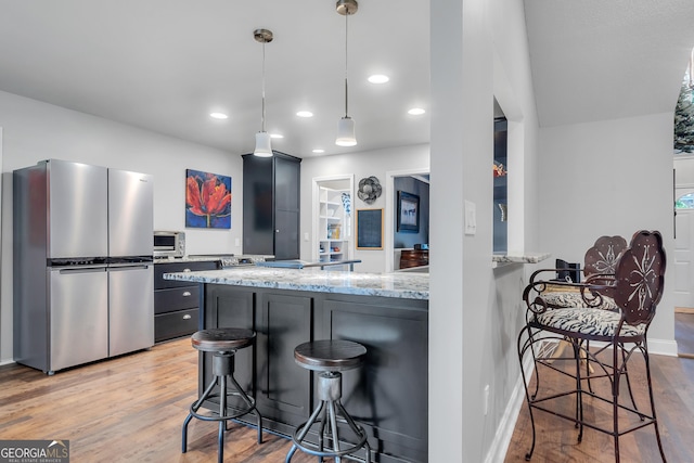 kitchen with light stone counters, a peninsula, freestanding refrigerator, a kitchen bar, and decorative light fixtures