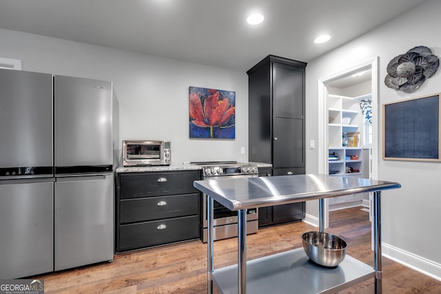 kitchen featuring a toaster, stainless steel appliances, light countertops, light wood-style flooring, and dark cabinetry