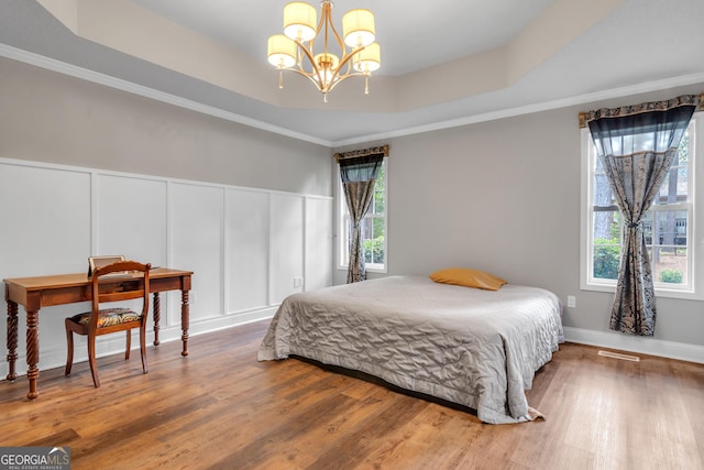 bedroom with a notable chandelier, wood finished floors, a raised ceiling, and a decorative wall