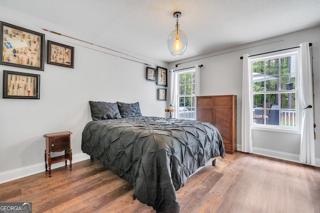 bedroom featuring a textured ceiling, baseboards, and wood finished floors